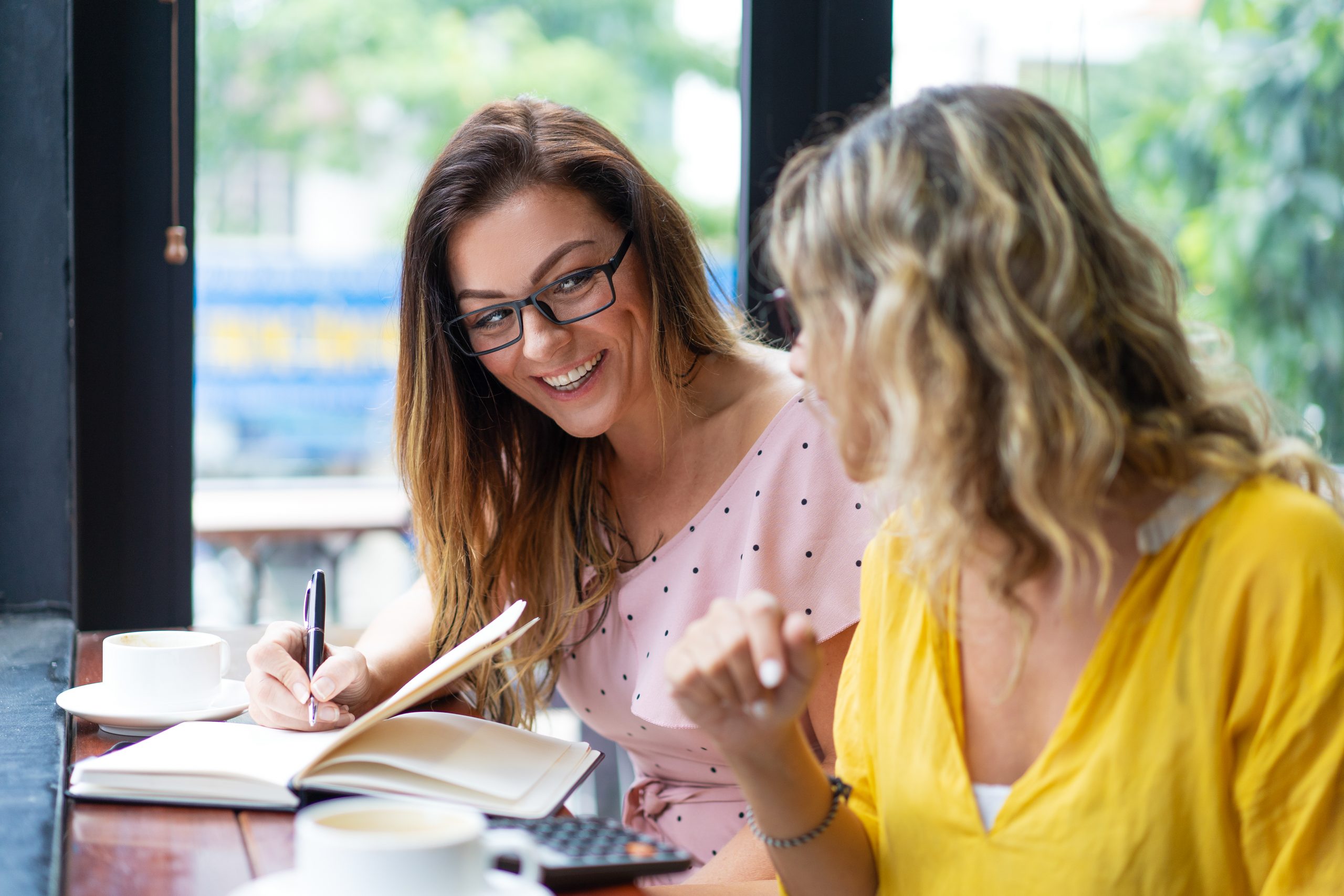 Happy women drinking coffee and working in cafe. Ladies sitting at table and using calculator. Women friendship and work concept.