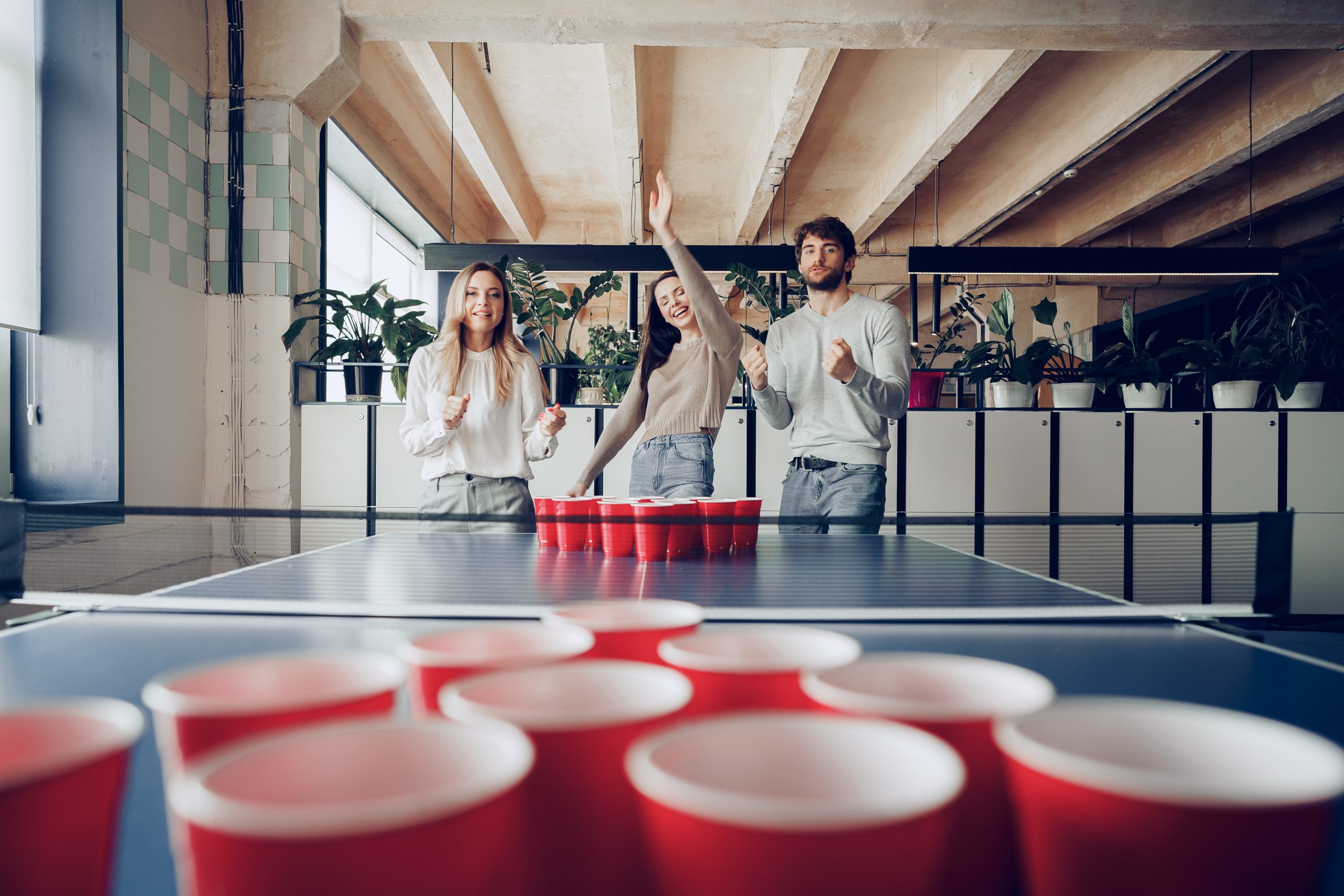 Young people coworkers playing beer pong game in modern office