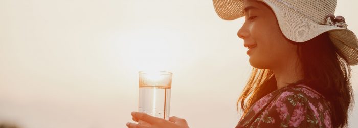 A girl wearing a red floral dress and a hat holding a glass of water with a light background in the sky...