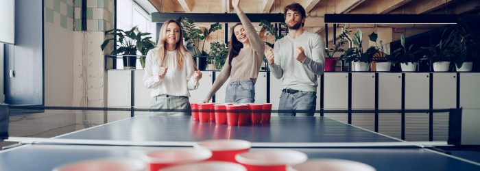Young people coworkers playing beer pong game in modern office