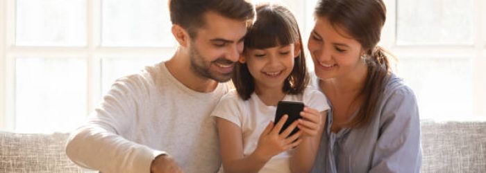Little kid daughter holding cellphone enjoy using mobile app, happy family with child having fun with smartphone device make online call looking at phone screen, shop in application at home on couch