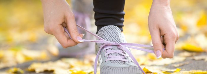Hands tying trainers shoelaces on the autumn pave, full of yellow leaves. Concept photo, horizontal, closeup