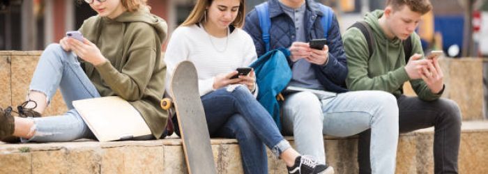 Four teenagers chatting on their smartphone on walking