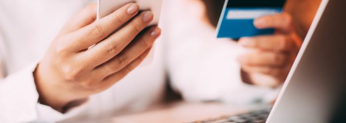 Close-up of female hand holding smartphone. Young businesswoman sitting at laptop in office holding credit card and entering data on her mobile phone