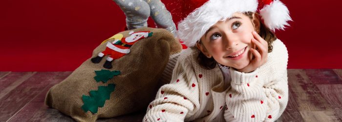 Adorable little girl wearing santa hat writing Santa letter on wooden floor. Winter clothes for Christmas.