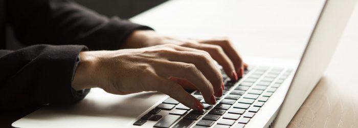 Close-up of female hands typing on laptop at table. Businesswoman working in office
