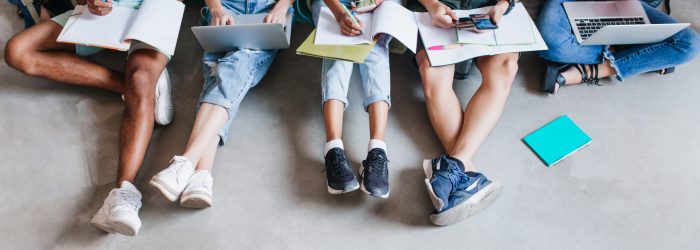 Overhead portrait of students in trendy sneakers chilling on the floor while preparing for exams together. University friends spending time together using laptops and writing abstract.