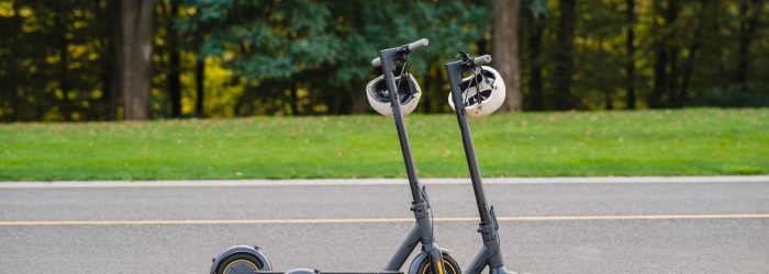 two electric kick scooters or e-scooter parked on the sidelines road in the park