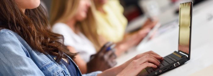 Young woman studying with laptop computer on white desk. Beautiful girls and guys working together wearing casual clothes. Multi-ethnic coworkers group.